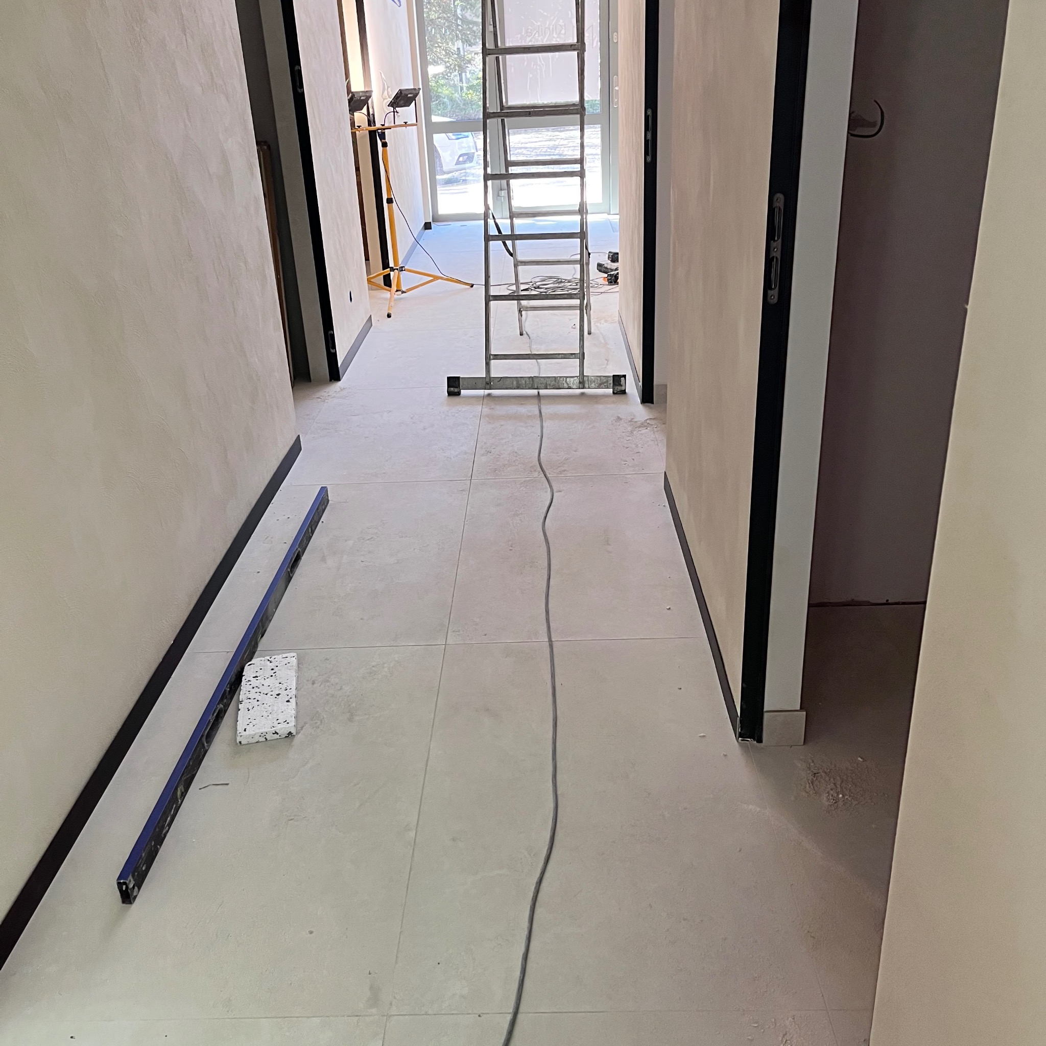 Wnętrze w trakcie wykończenia: gładkie ściany, jasna podłoga, drabina w przejściu. Widoczne narzędzia i kabel. Minimalistyczny styl w trakcie realizacji.