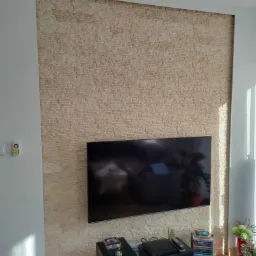 Ściana akcentowa z dekoracyjnej cegły w salonie, z zawieszonym telewizorem i sprzętem audio, oświetlona naturalnym światłem.