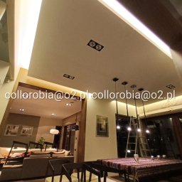 Collorobia Marek Czub - Nowoczesne oświetlenie LED w suficie podwieszanym, widok na jadalnię z ciemnymi krzesłami i stołem z wzorzystym obrusem, w tle salon z sofą i dekoracjami ściennymi, drabina oparta o okno.