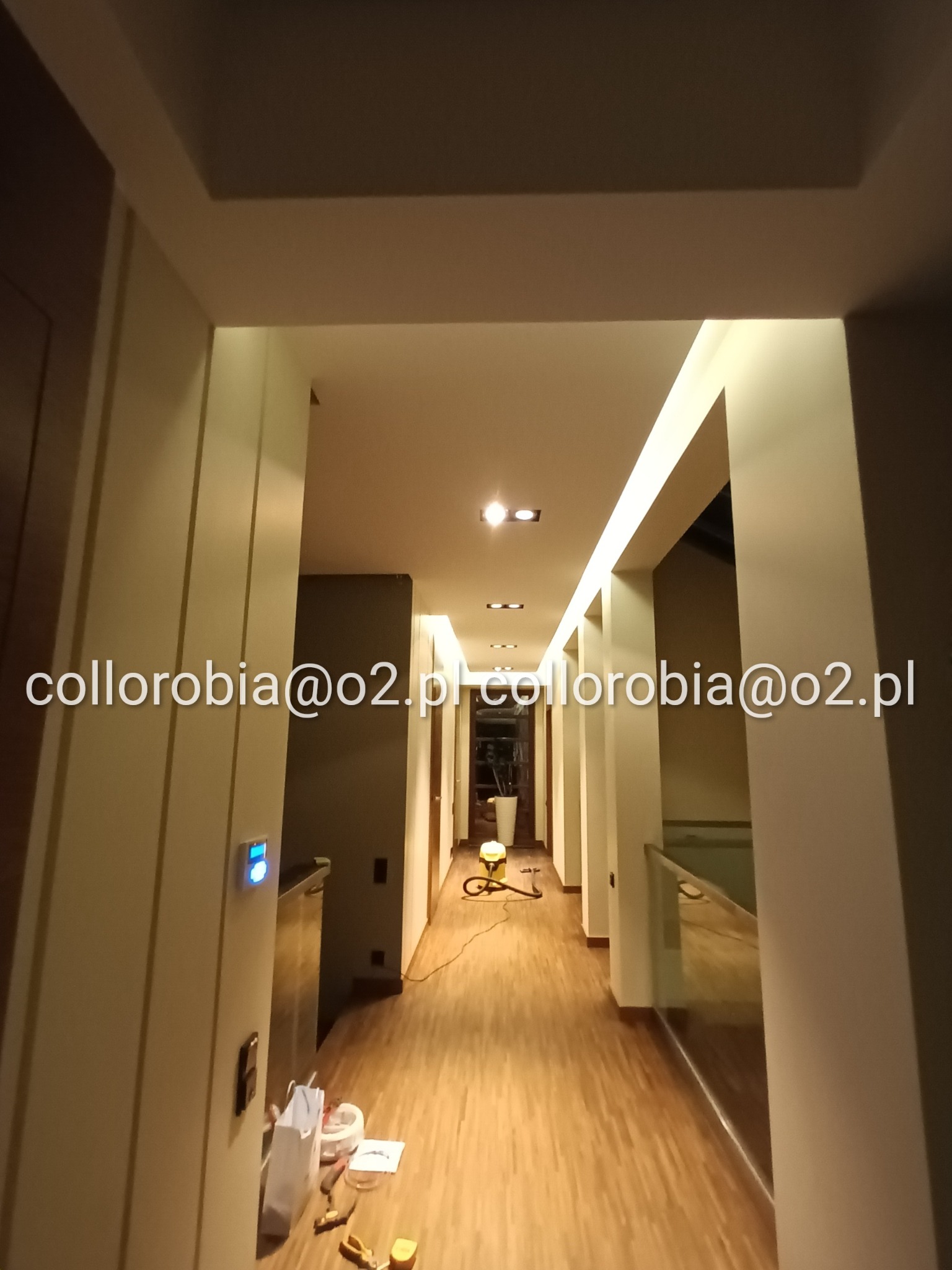 Korytarz z zamontowanym oświetleniem LED w listwach sufitowych, widoczny parkiet oraz narzędzia na podłodze podczas montażu.