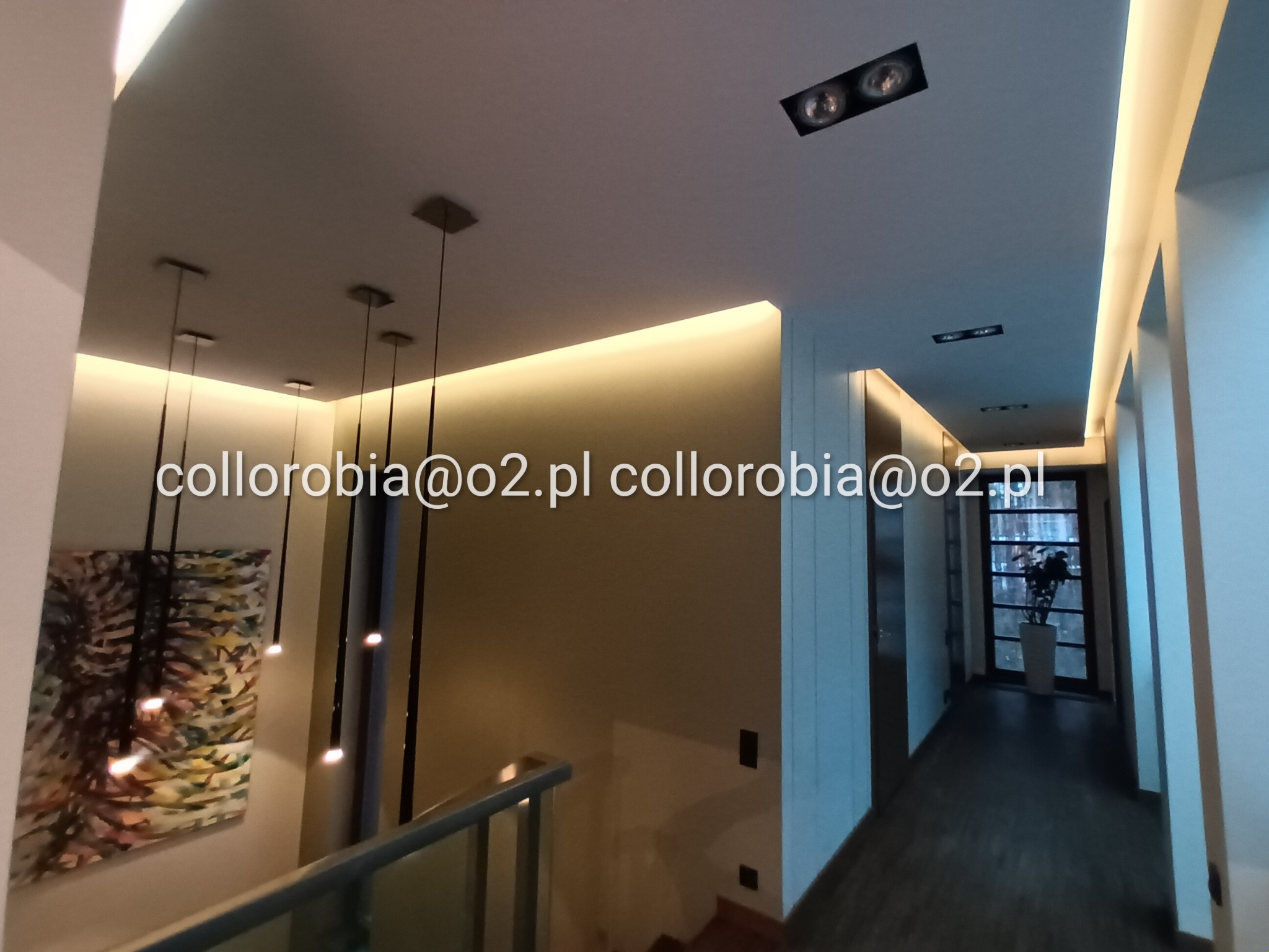 Nowoczesne oświetlenie LED w korytarzu z wiszącymi lampami i podświetleniem sufitowym, widok z góry schodów z balustradą.