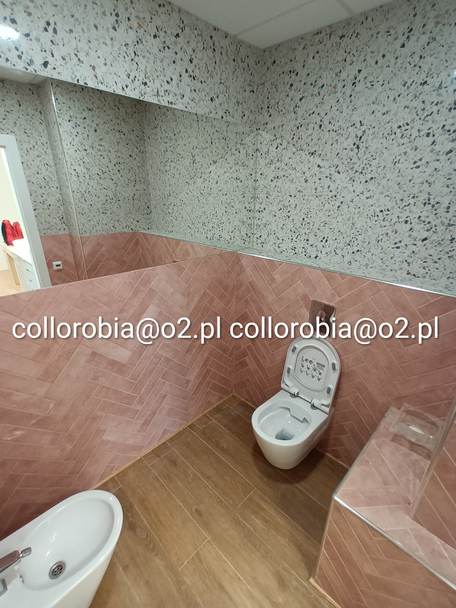 Wykończona łazienka z toaletą, bidetem i kabiną prysznicową, ściany wyłożone płytkami w jodełkę w odcieniach różu, podłoga imitująca drewno, ściana nad płytkami wykończona mozaiką.