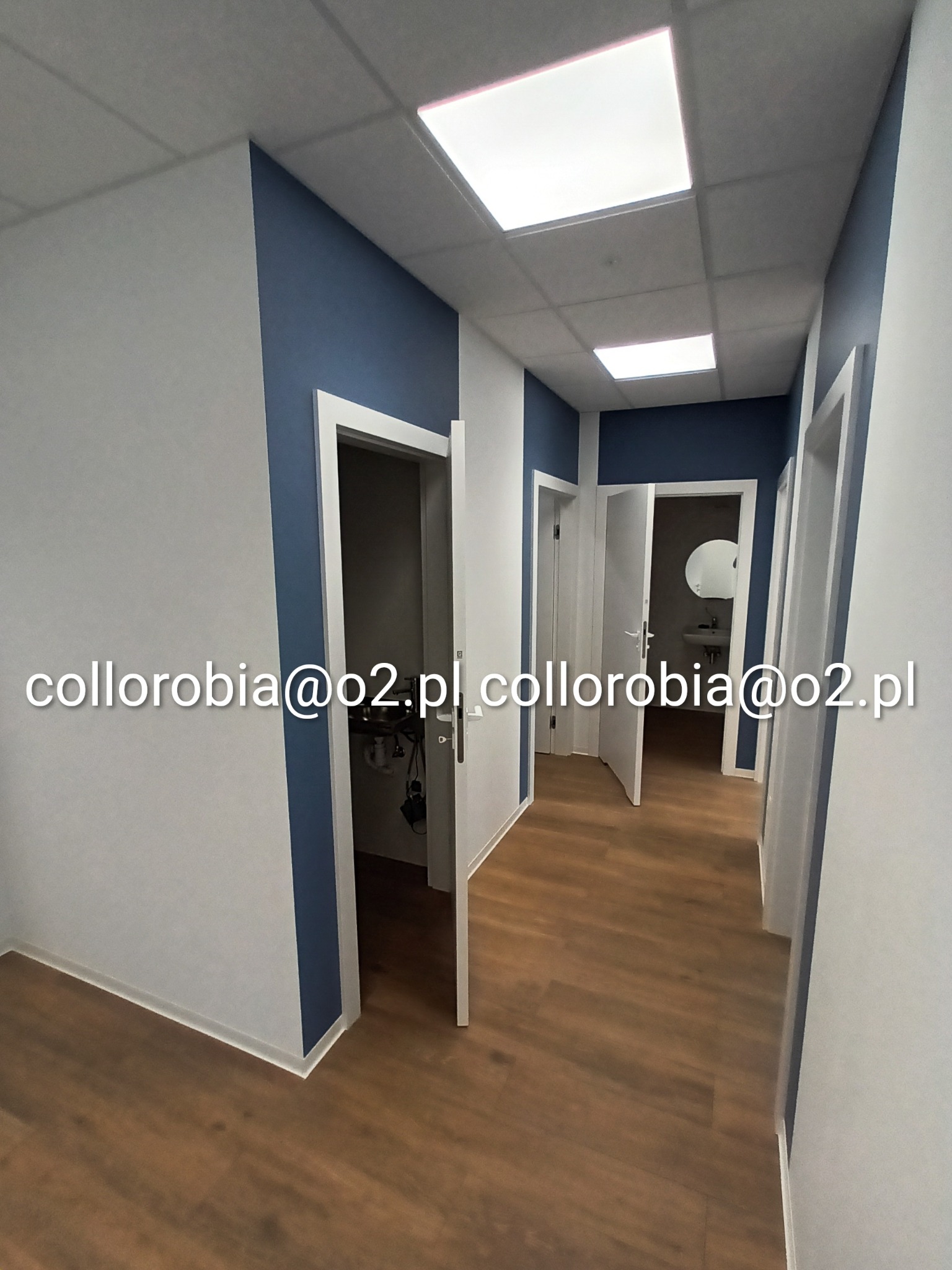 Korytarz biurowy po odświeżeniu, z brązowymi panelami podłogowymi, białymi ścianami z granatowymi akcentami i białymi ościeżnicami, widok na umywalkę i lustro w łazience.