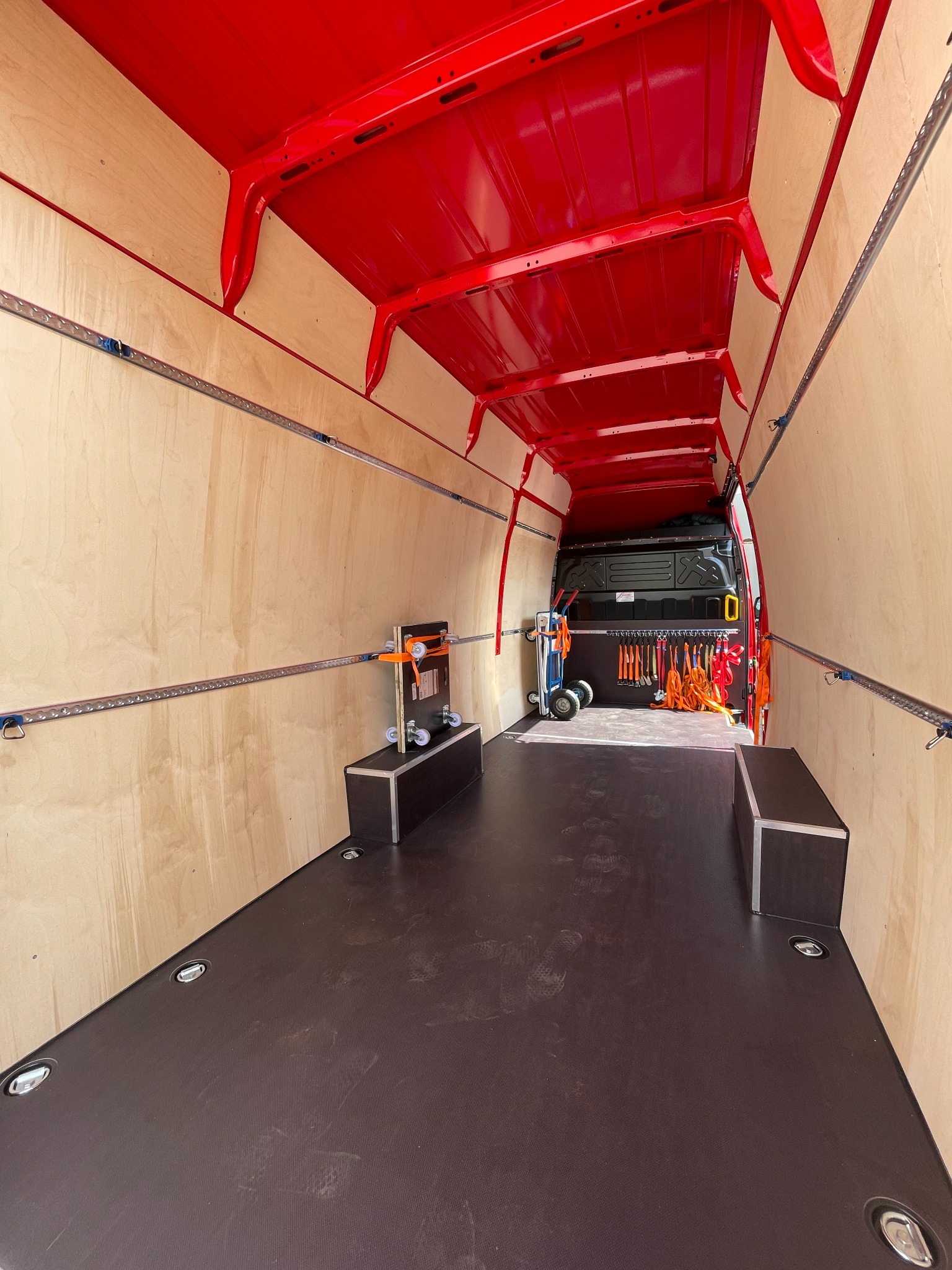 Wnętrze pustego, wyłożonego sklejką i zabezpieczonego szynami transportowymi, czerwonego busa dostawczego, przygotowanego do transportu ładunków.