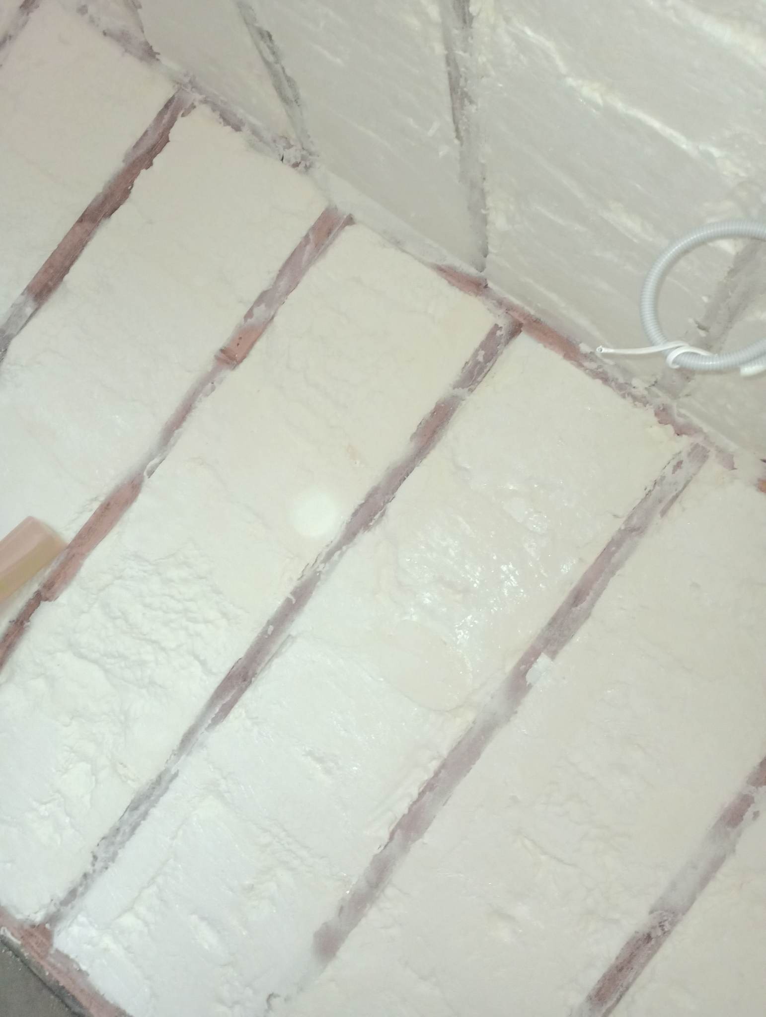 Poddasze z drewnianą konstrukcją pokryte warstwą jasnej pianki izolacyjnej, widoczne przewody elektryczne.