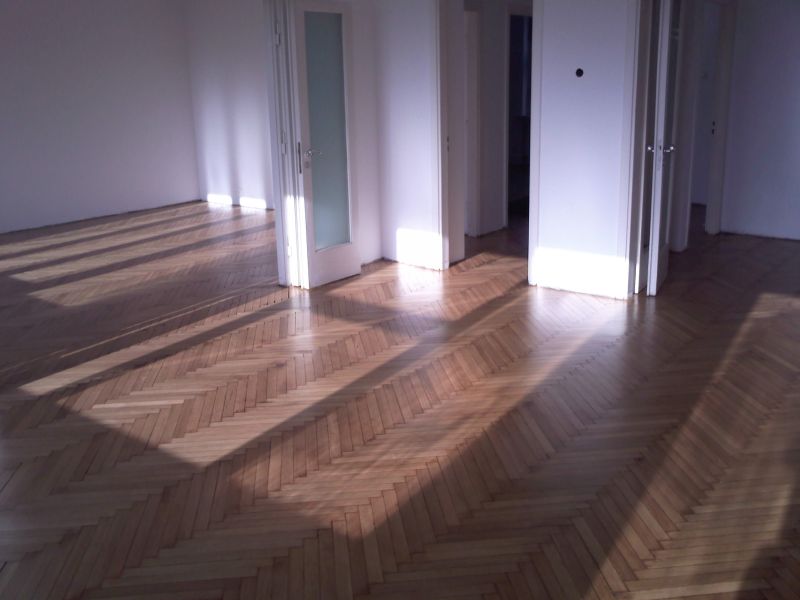 Parkiet ułożony w jodełkę po cyklinowaniu, z widocznymi promieniami słońca wpadającymi przez okno, podkreślającymi strukturę drewna i gładką powierzchnię.