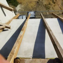 Wysoki kąt widzenia na fundamenty domu murowanego z widocznymi drewnianymi belkami, siatką wzmacniającą i częściowo ułożonymi bloczkami betonowymi.