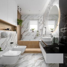 Dobry Dom Invest - Nowoczesna łazienka z marmurowymi płytkami, wiszącą toaletą i bidetem, owalnym lustrem z podświetleniem LED oraz czarnym blatem z umywalką.