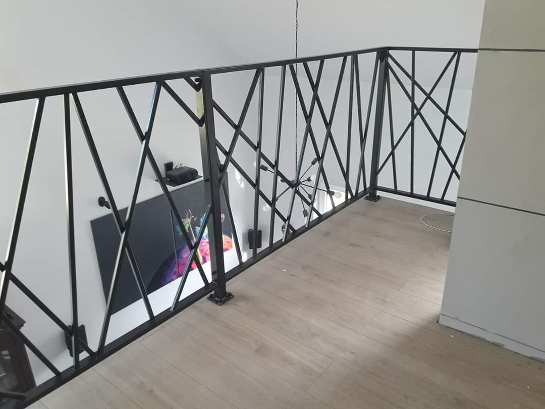 Czarna, metalowa balustrada o geometrycznym wzorze na antresoli z panelami podłogowymi, widok z góry.