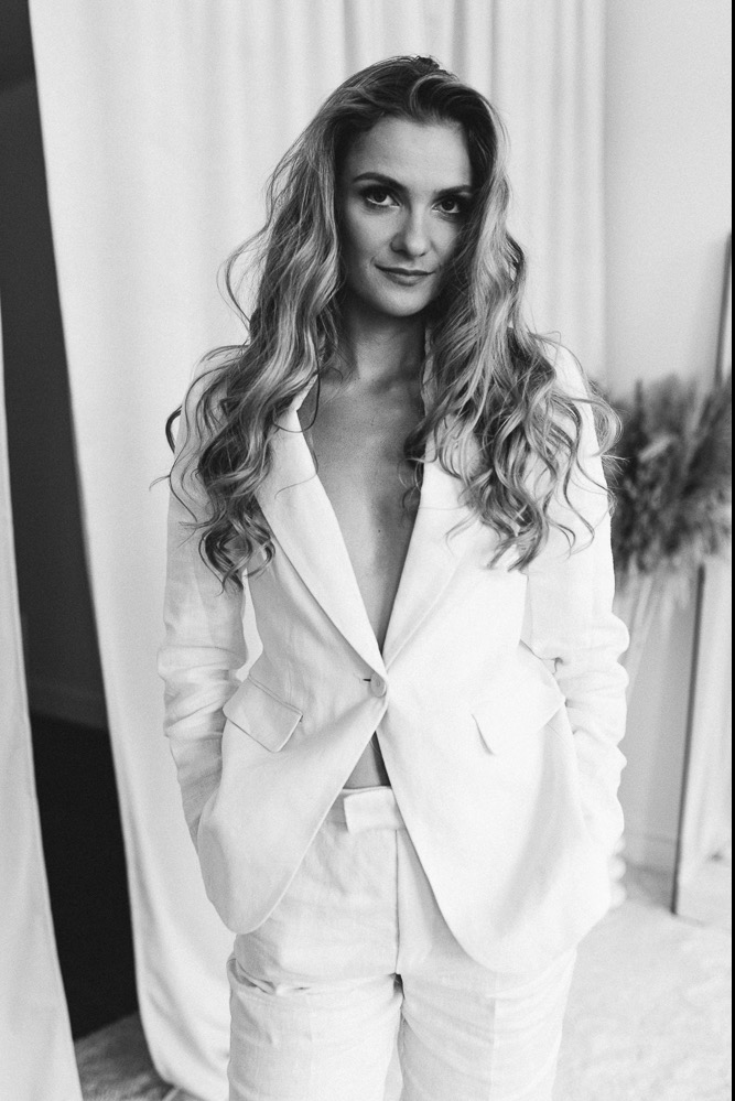 Portret kobiety w białym lnianym garniturze, z rozpuszczonymi włosami, na jasnym tle.