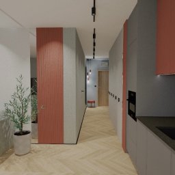 COLIBRIART PRACOWNIA WNĘTRZ EWA ŚWIDERSKA-BASIAK - Wnętrze mieszkania z sofą, rośliną i kuchnią z niebieskimi płytkami. Widok na korytarz z oświetleniem punktowym. Projekt w odcieniach szarości i koralowej czerwieni.