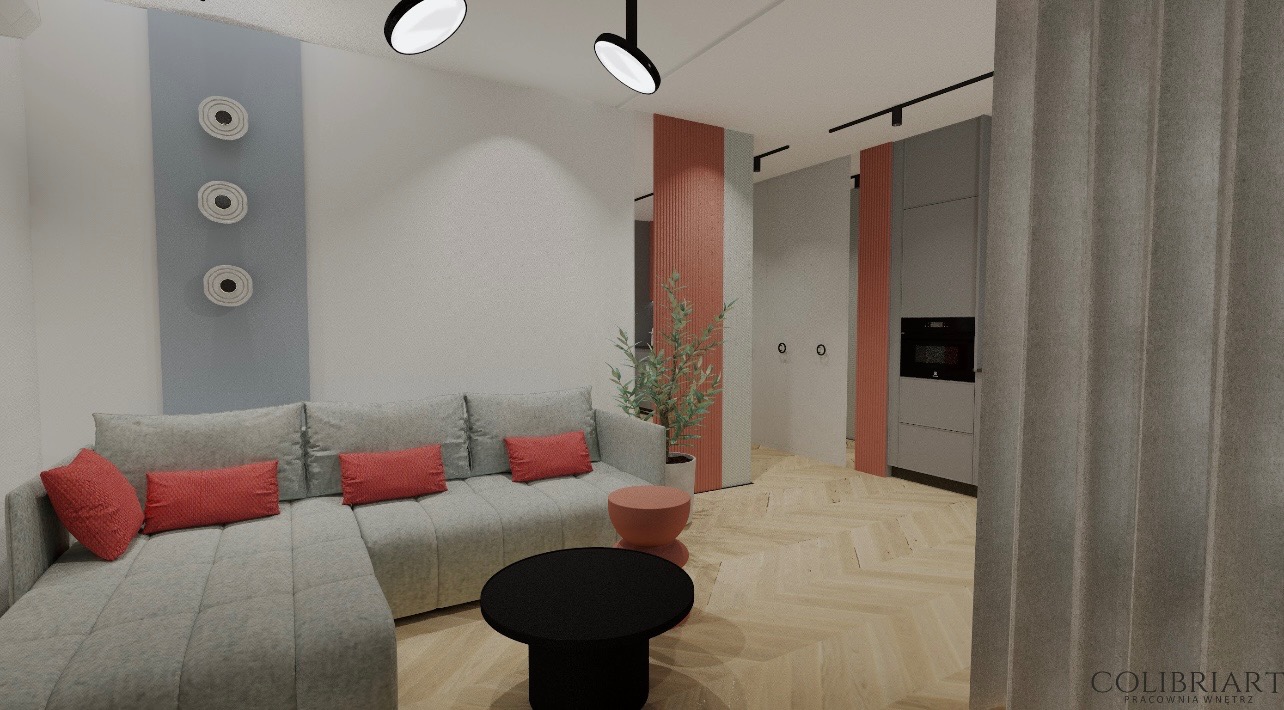 Stylowy salon z szarą sofą, czerwonymi poduszkami i okrągłym stolikiem kawowym. Na ścianie dekoracyjne talerze. Widoczna kuchnia w tle. Parkiet w jodełkę.