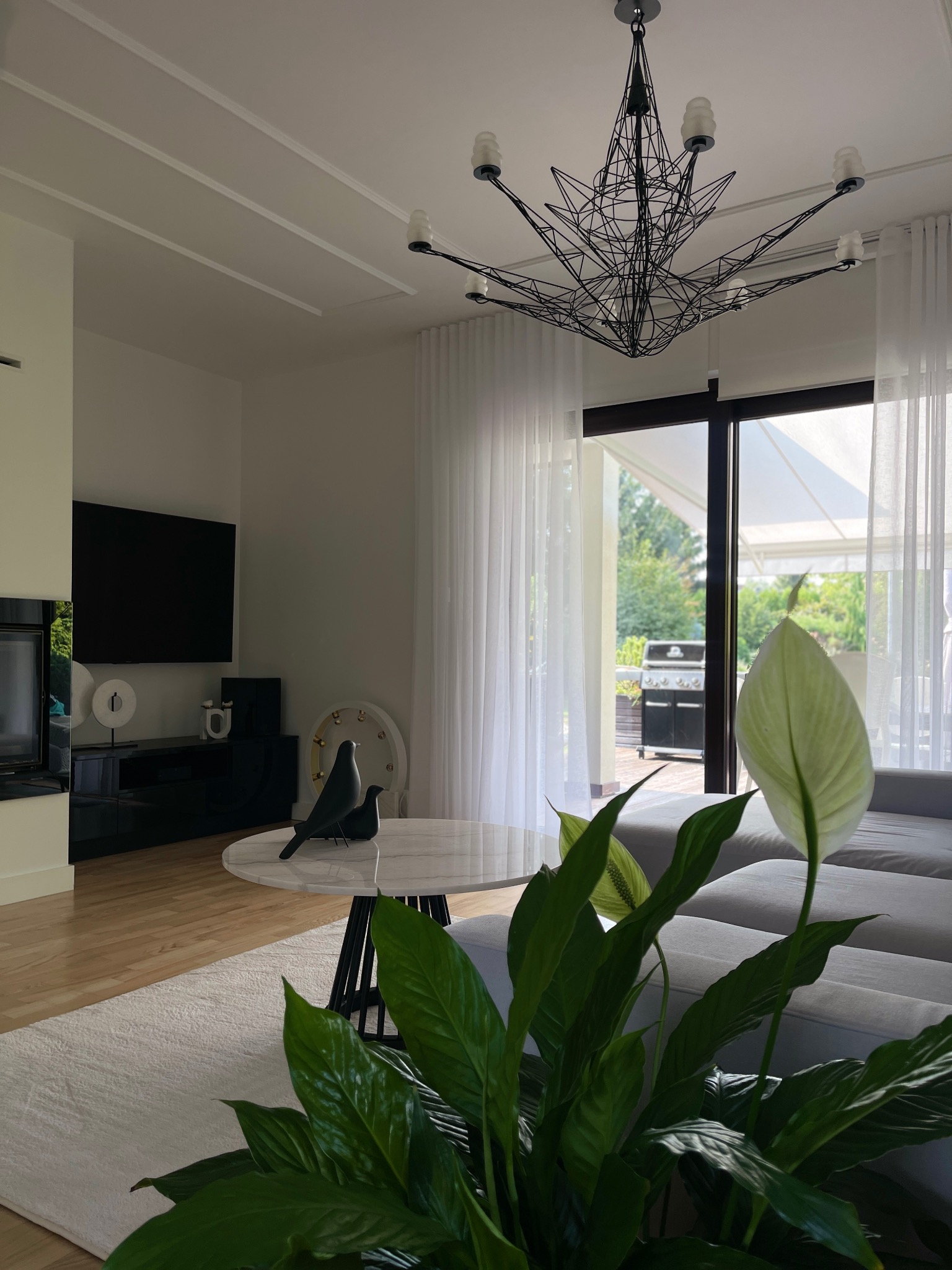 Nowoczesny salon w Kielcach z marmurowym stolikiem, designerską lampą i widokiem na ogród przez przeszklone drzwi balkonowe. Minimalistyczny wystrój z akcentem roślinnym.