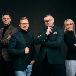 Zespół czterech osób w eleganckich marynarkach pozuje na ciemnym tle: mężczyzna w brązowym tweedzie, mężczyzna w zielono-niebieskiej kracie, mężczyzna z chusteczką w kieszonce i kobieta w czarnej...