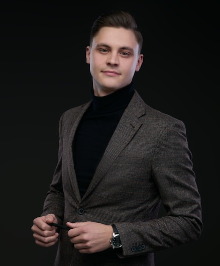 Portret mężczyzny w brązowym garniturze i czarnym golfie na ciemnym tle, z zegarkiem na ręce, prezentujący się jako doradca finansowy we Wrocławiu.