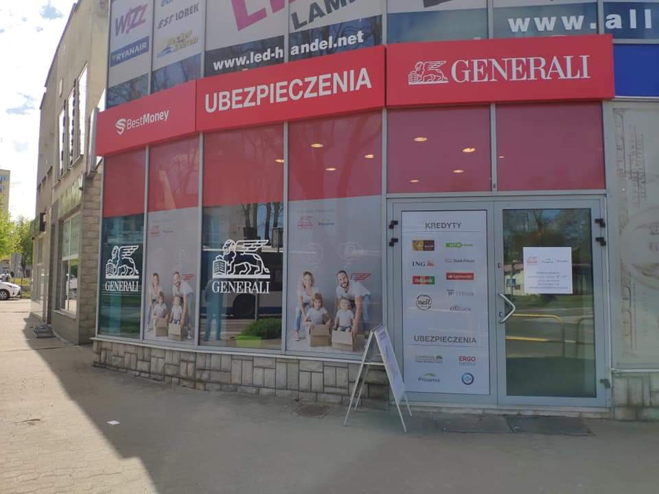 Fasada budynku z biurem firmy ubezpieczeniowej Generali, widoczne logo i napisy Ubezpieczenia, BestMoney, Kredyty oraz naklejki z logo innych firm finansowych na drzwiach.