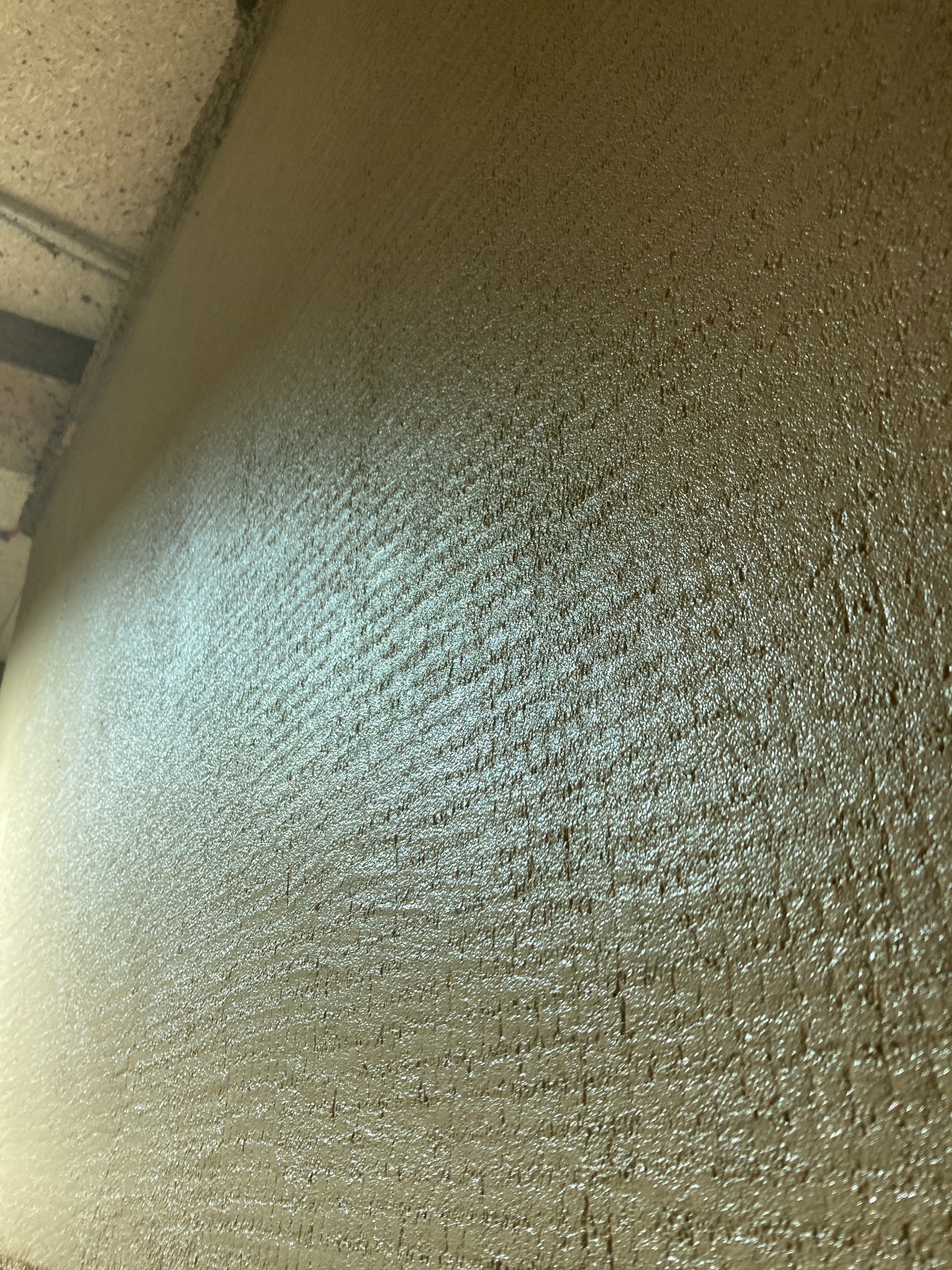 Świeżo nałożona, mokra warstwa tynku z wyraźną fakturą na ścianie i suficie, widoczne ślady po narzędziu, oświetlenie podkreśla nierówności powierzchni.