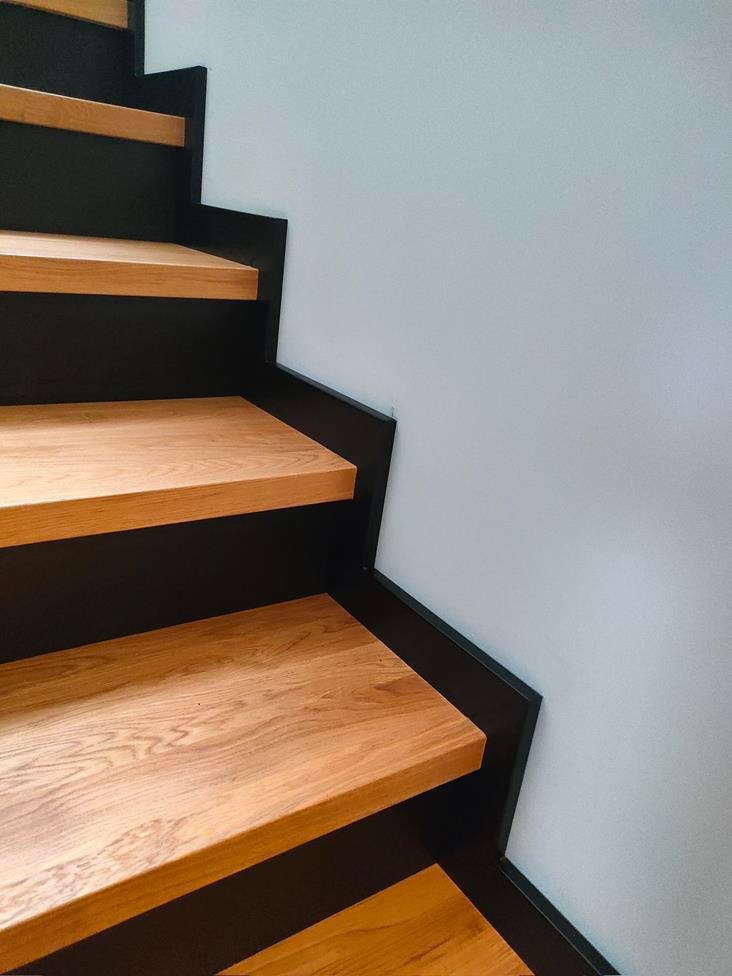 Nowoczesne schody z drewnianymi stopniami i czarną konstrukcją, widok z dołu.