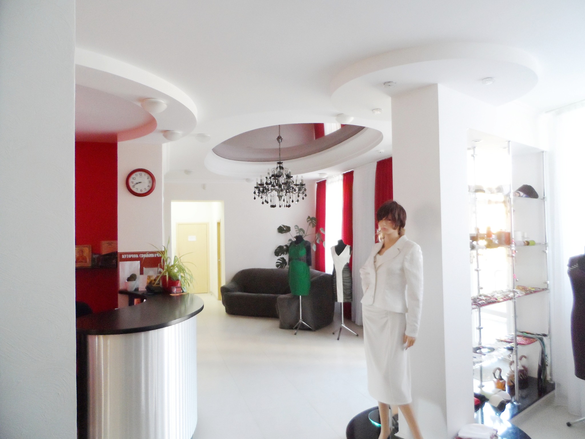 Jasne, przestronne wnętrze butiku z recepcją, manekinami prezentującymi ubrania i dekoracyjnym oświetleniem sufitowym.