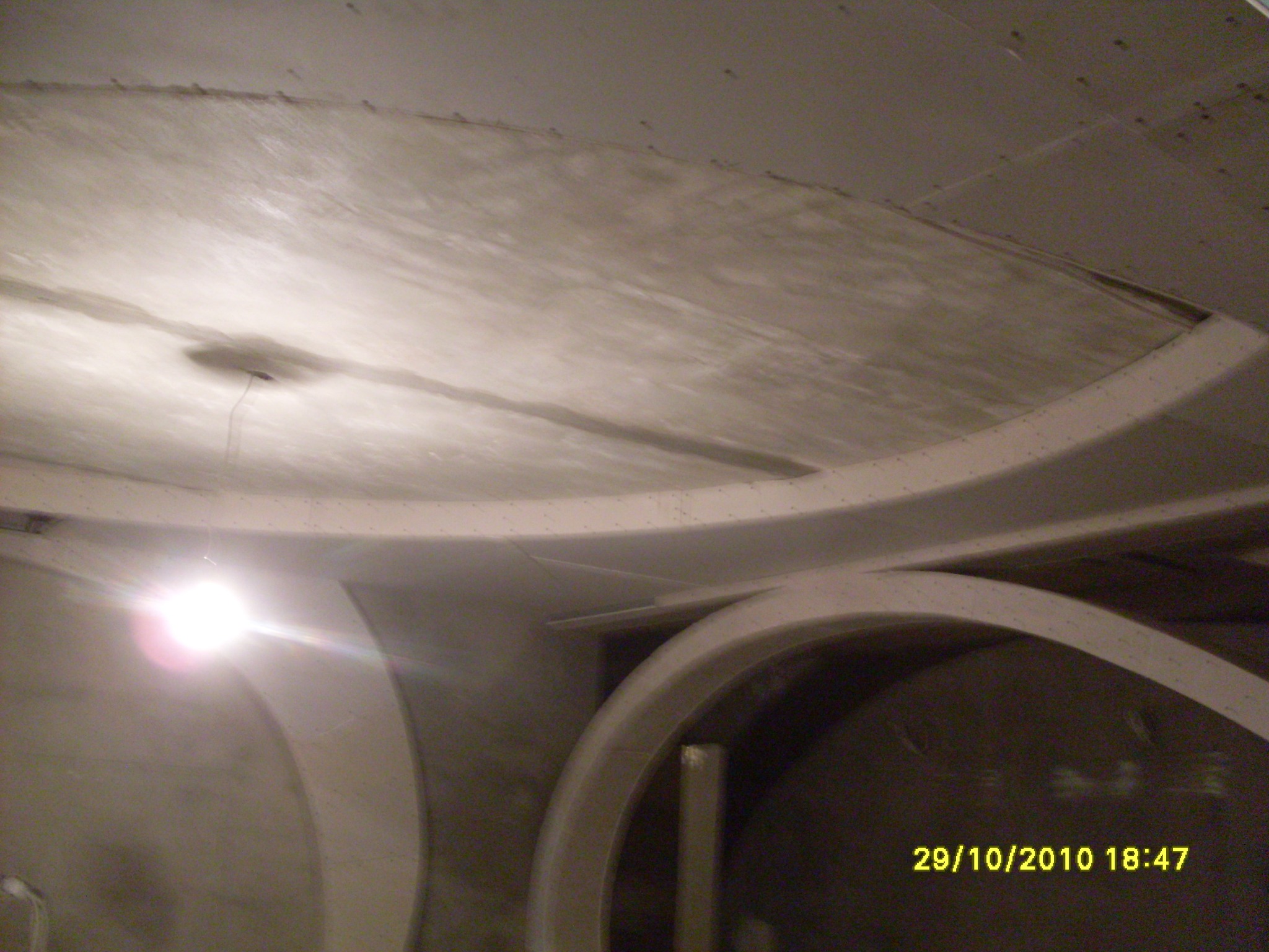 Niedokończone sklepienie z widocznymi elementami konstrukcyjnymi i surową powierzchnią, oświetlone punktowo.