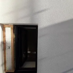 Montaż okna w elewacji z widoczną warstwą izolacji termicznej i drewnianą ramą pomocniczą.