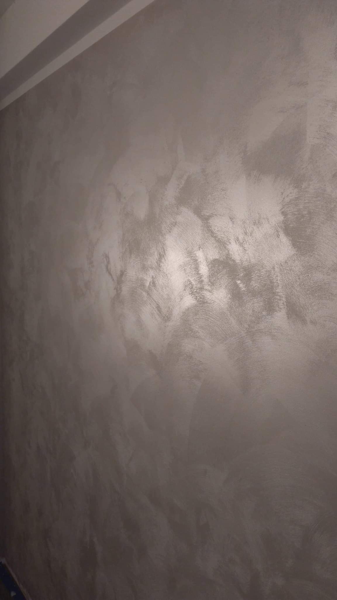 Ściana pokryta dekoracyjną, szarą strukturą z widocznymi śladami pędzla lub szpachli, tworzącymi efekt subtelnych smug i cieni.