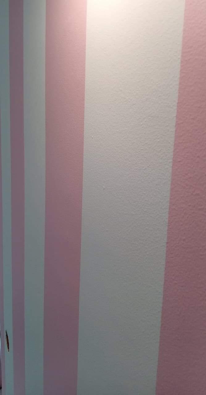 Równo pomalowana ściana w pionowe pasy w odcieniach różu i bieli, widoczna delikatna struktura farby.