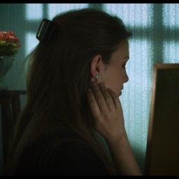 Bohema Pictures - Profil kobiety z upiętymi włosami, dotykającej twarzy, w tle wazon z kwiatami i rama obrazu, oświetlona przez padające cienie na wzorzystej tapecie.