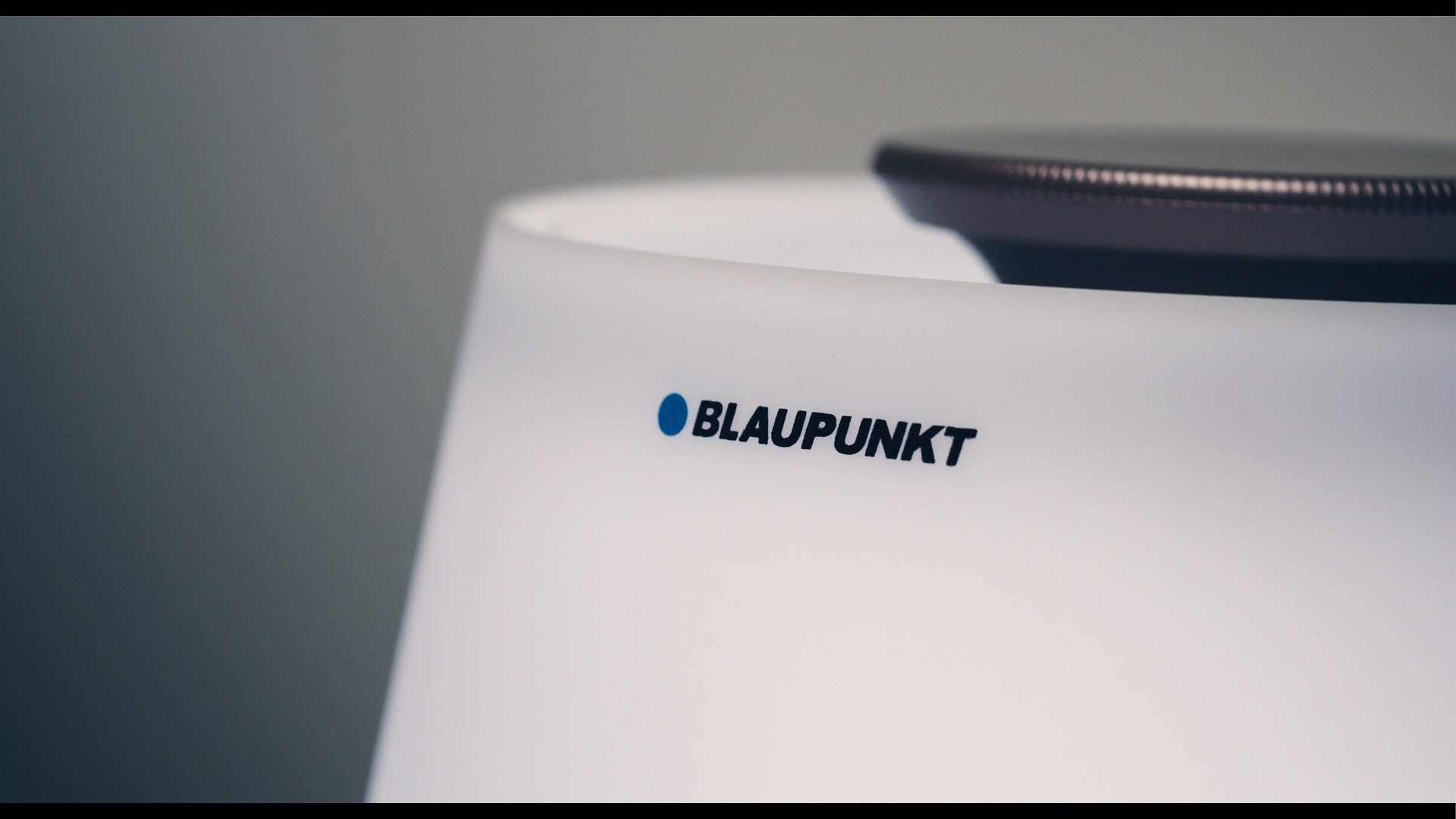 Zbliżenie na biały, cylindryczny głośnik marki Blaupunkt z widocznym logo na tle szarej ściany.