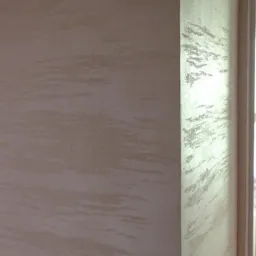 Ściana wewnętrzna z dekoracyjnym, beżowym malowaniem imitującym smugi, widoczny narożnik i fragment ramy okiennej.