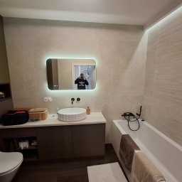 Pro-Home - Nowoczesna łazienka z podświetlanym lustrem, umywalką na szafce i wanną z czarną armaturą. Beżowe płytki na ścianach i ciemna podłoga tworzą elegancki kontrast.