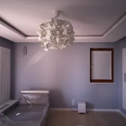 Jasny pokój z szarymi ścianami, drewnianą podłogą i nowoczesną lampą sufitową, sofa zabezpieczona folią ochronną, okno z drewnianą ramą, białe listwy przypodłogowe.