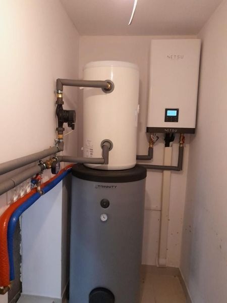 Zestaw instalacji grzewczej z zasobnikiem i jednostką zewnętrzną Netsu, zamontowany w pomieszczeniu technicznym w Legnicy, z widocznymi rurami w izolacji.