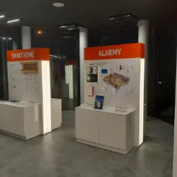 Ekspozycja systemów alarmowych i inteligentnego domu w salonie, prezentacja urządzeń Satel na białych szafkach z podświetleniem.