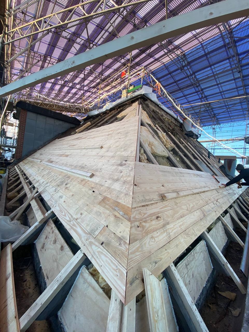 Konstrukcja drewniana dachu w trakcie budowy, widoczne izolacja i rusztowanie ochronne, z bliska na pierwszym planie ułożone deski.