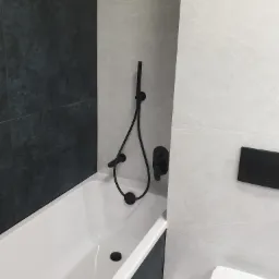 Nowoczesna łazienka z białą wanną, czarną armaturą i szaro-białymi płytkami imitującymi marmur.