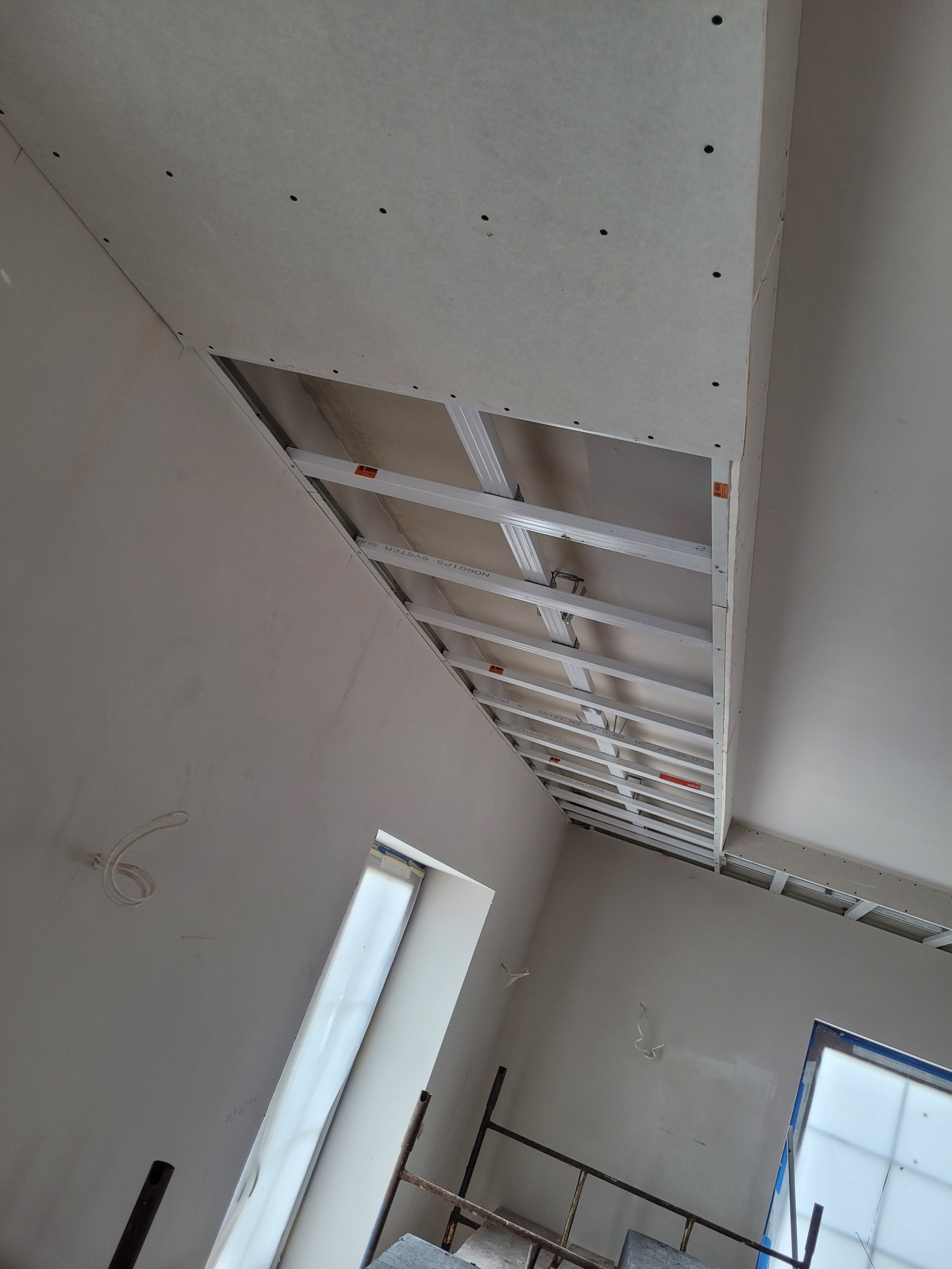 Widok na sufit podwieszany w trakcie montażu: widoczne płyty gipsowo-kartonowe z widocznymi otworami po wkrętach oraz metalowa konstrukcja nośna.