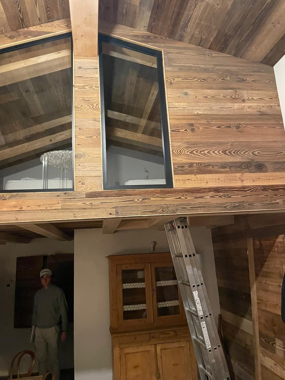 Wnętrze domu w Białymstoku z drewnianą boazerią, widoczne okna dachowe z czarnymi ramami, antresola z widocznym oświetleniem oraz drabina oparta o ścianę, sugerująca trwające prace wykończeniowe.