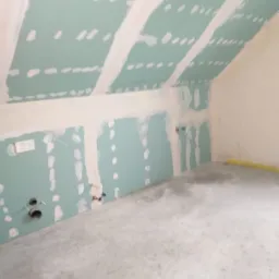 Poddasze z zamontowanymi płytami karton gips, widoczne łączenia płyt zaszpachlowane, instalacja elektryczna i rury kanalizacyjne wystają ze ściany.