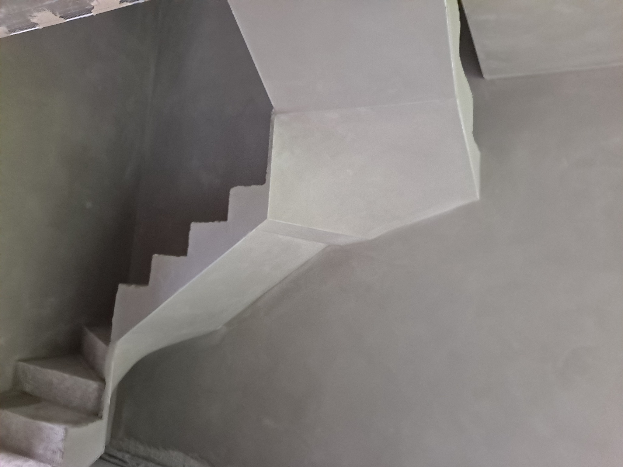 Surowe schody wewnętrzne po nałożeniu warstwy tynku, widoczne niedoskonałości i szarość koloru.