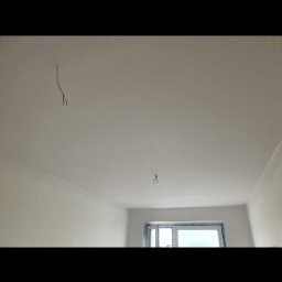 Kompleksowe wykończenia wnętrz Łukasz Sawicki - Pomalowane na biało wnętrze pokoju z wystającymi przewodami z sufitu i oknem w tle.