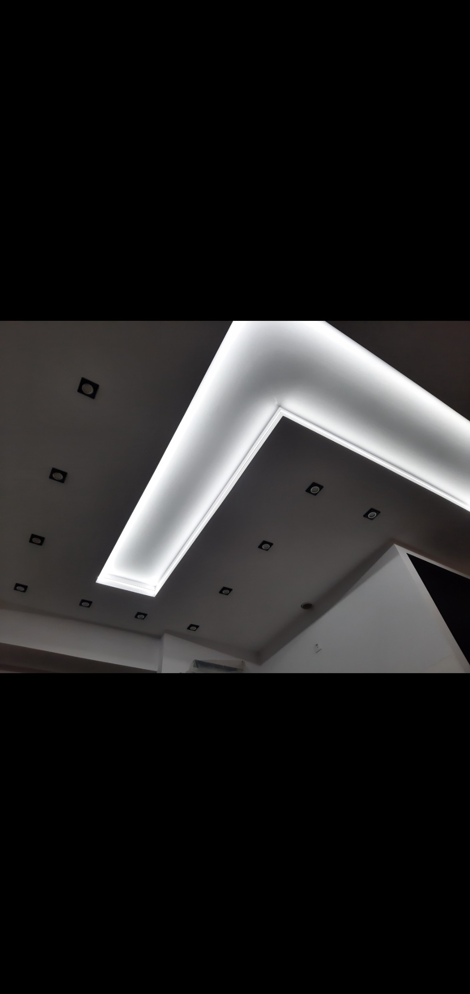 Sufit podwieszany z oświetleniem LED w kształcie litery L, z punktowymi lampami wpuszczanymi, widok z dołu.