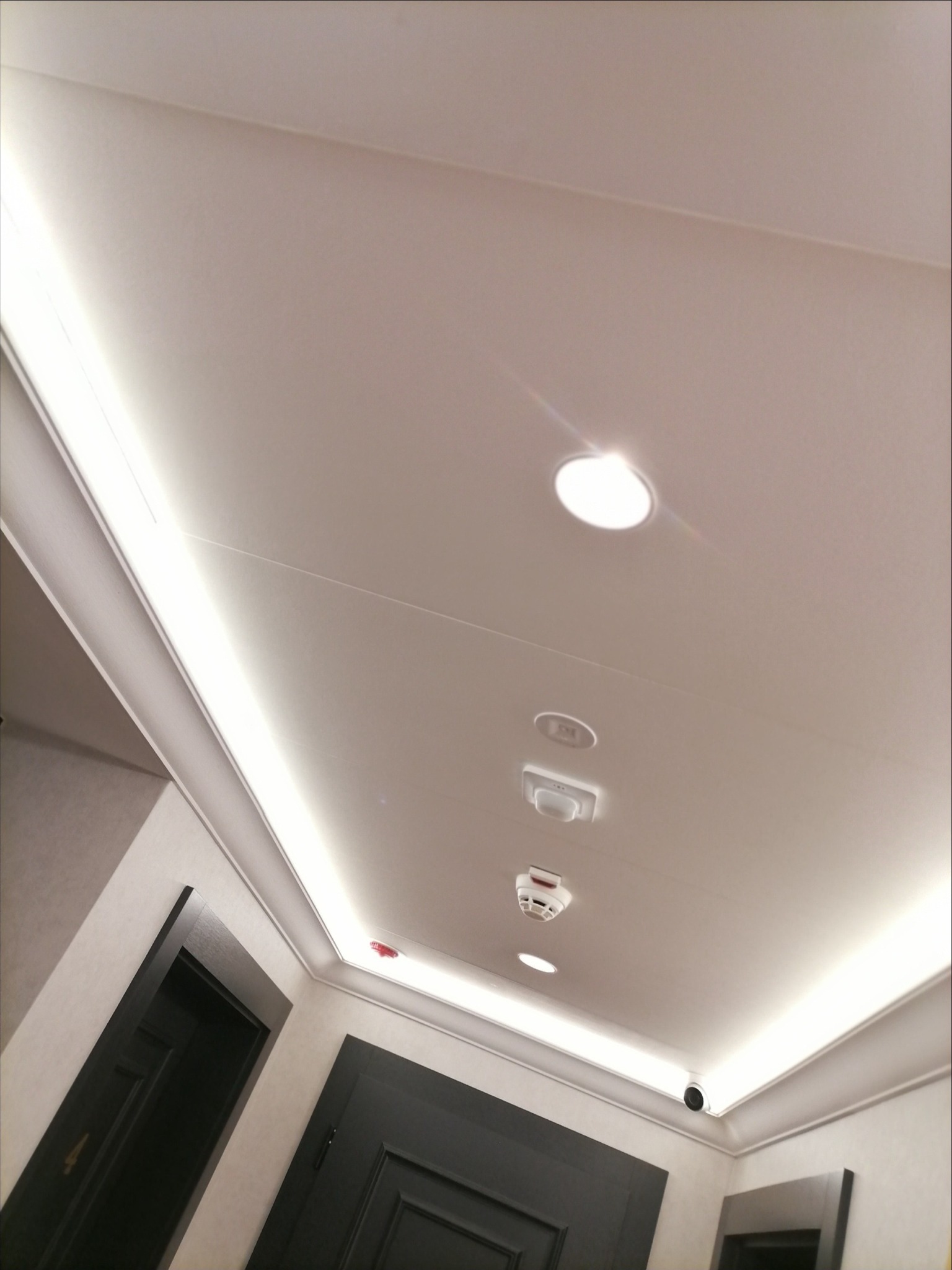 Nowoczesny sufit z oświetleniem LED, czujnikiem dymu i kamerą bezpieczeństwa, widok z dołu.