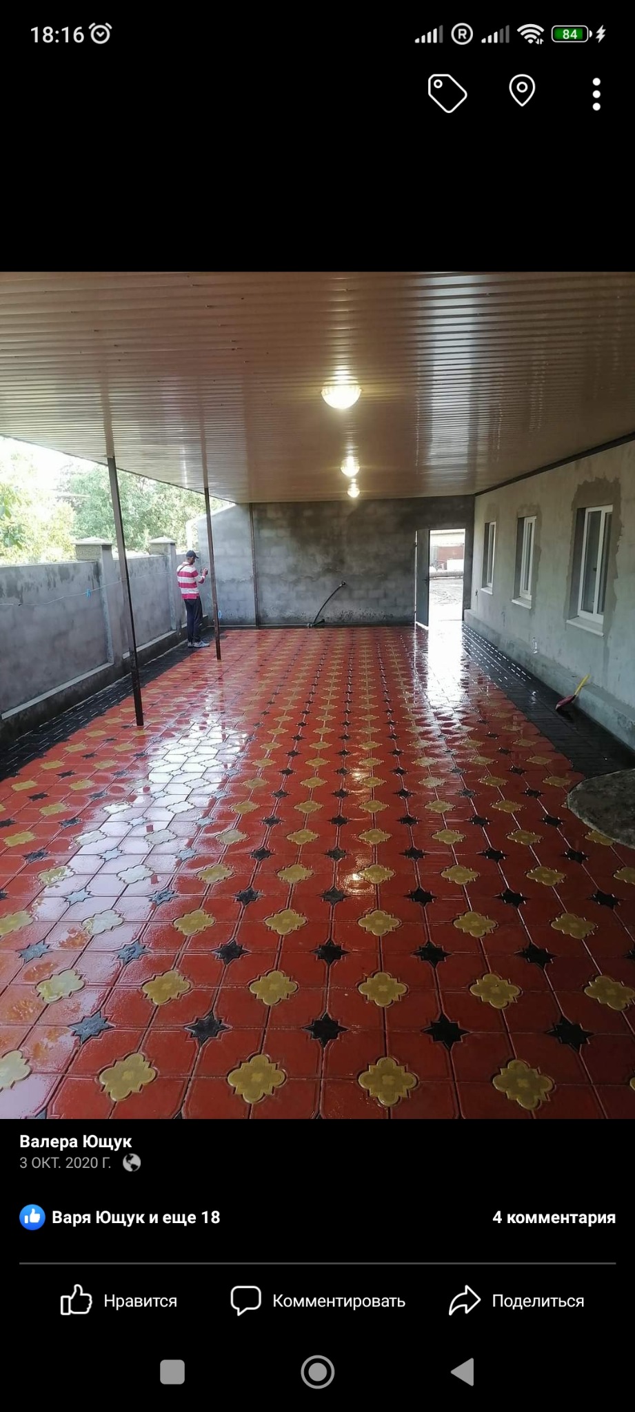 Świeżo ułożona, błyszcząca kostka brukowa w kolorach czerwonym, żółtym i czarnym na zadaszonym tarasie, widoczne ślady wilgoci po myciu, pracownik w oddali.