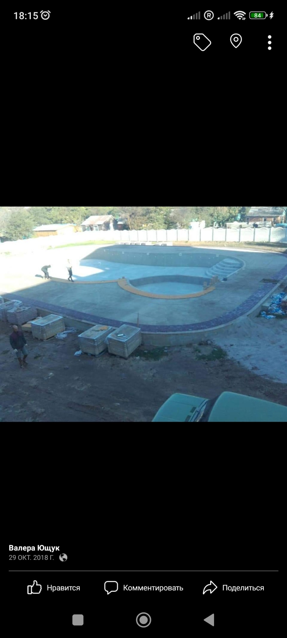 Budowa basenu z obrzeżem z kostki granitowej, widoczni pracownicy oraz palety z materiałem budowlanym.