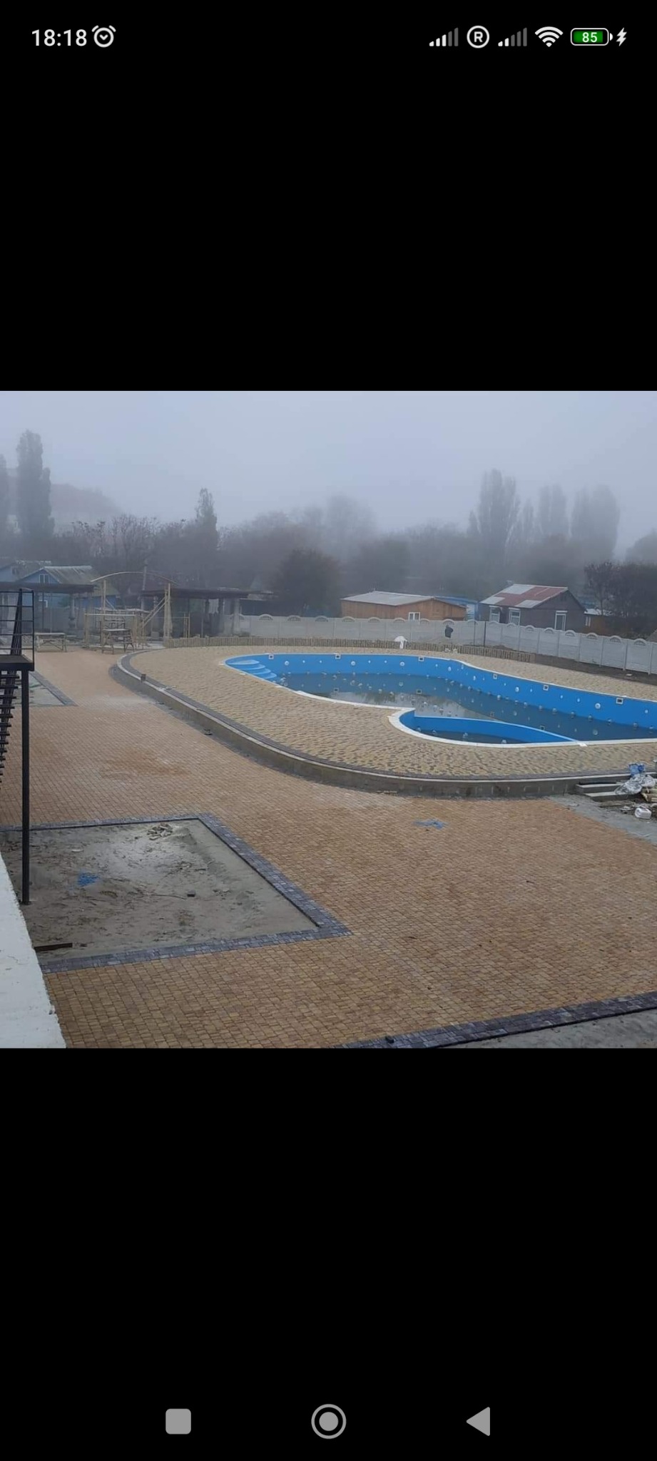 Widok z góry na nowo ułożoną, brązową kostkę wokół basenu w mglisty dzień. Fragment niezakończonej nawierzchni z kostki w lewym dolnym rogu.