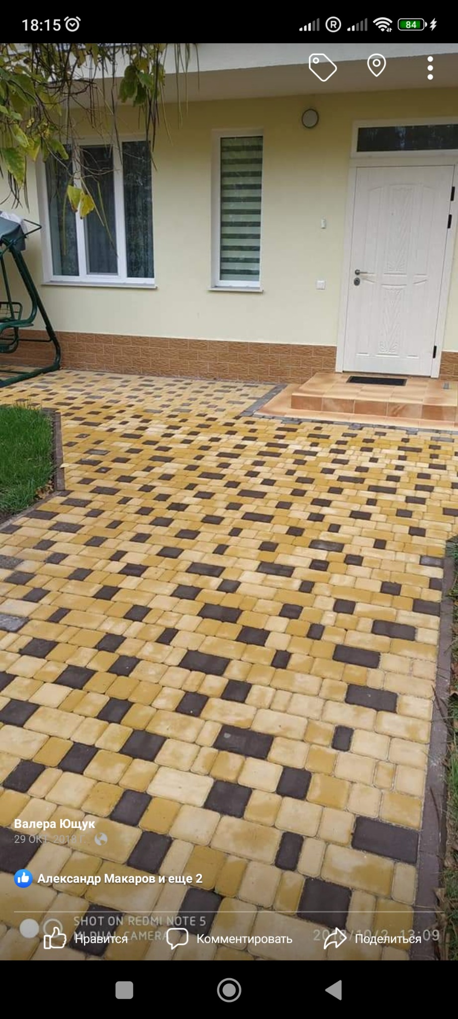 Ułożona kostka brukowa w kolorach żółtym i grafitowym prowadząca do wejścia domu z białymi drzwiami i oknami.