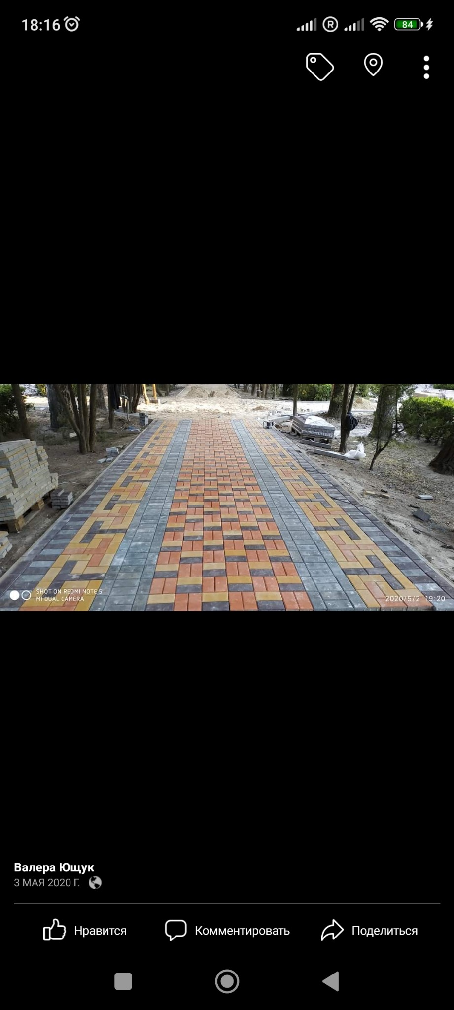 Szeroki chodnik z kostki brukowej w odcieniach czerwieni, żółci i szarości, prowadzący przez park, z ułożonymi kostkami po bokach, gotowymi do dalszej pracy.