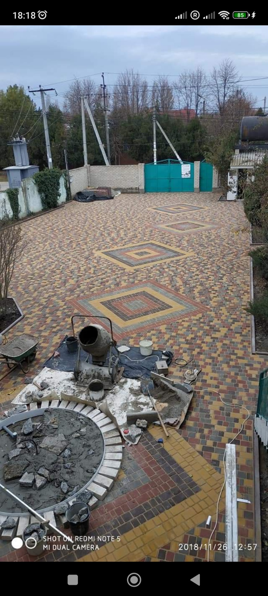 Układanie kostki brukowej w geometryczny wzór z kwadratami, widoczna betoniarka i rozpoczęty okrąg z kostki.