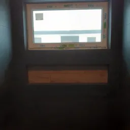 Ciemna łazienka z oknem VEKA i drewnopodobną półką wnękową, widoczne płytki imitujące drewno na podłodze i ścianach, pomarańczowe akcesoria na podłodze.